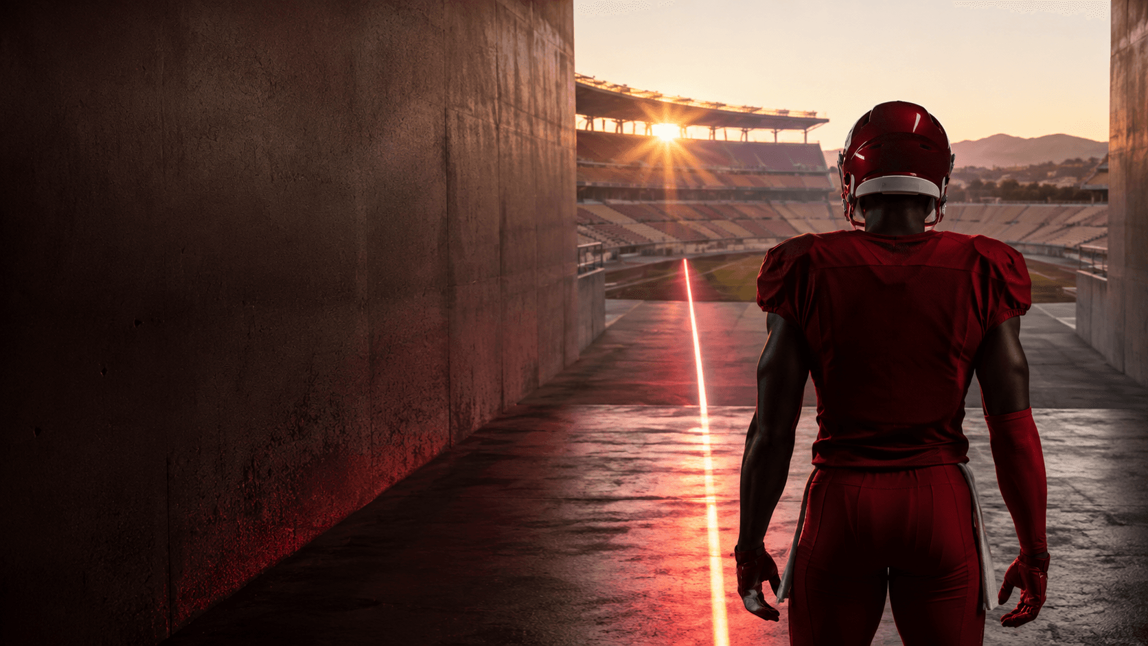 An anonymous receiver in a deep-red uniform stands in a desert stadium tunnel as a red line leads toward the field, symbolizing a long-term contract.
